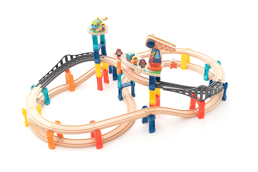 A sprawling wooden toy railway set laid out on a floor, with trains, bridges, and stations