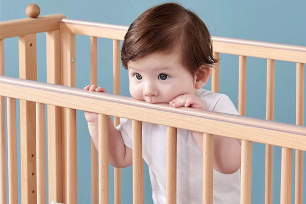 A toddler standing in a mini crib looking almost tall enough to climb out