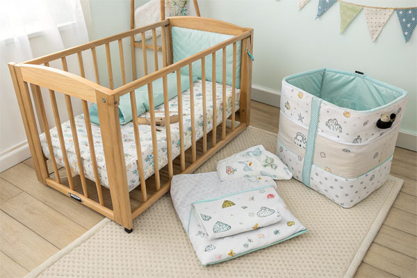 A wooden mini crib side-by-side with a fabric pack and play