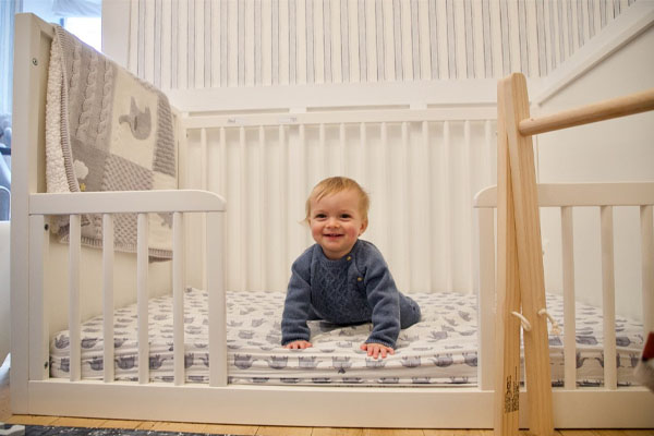 An image showing a traditional crib and a Montessori floor bed with an arrow pointing in opposite directions