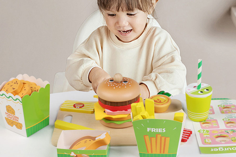 Two children playing together, one chopping a wooden carrot while the other stirs a pot.
